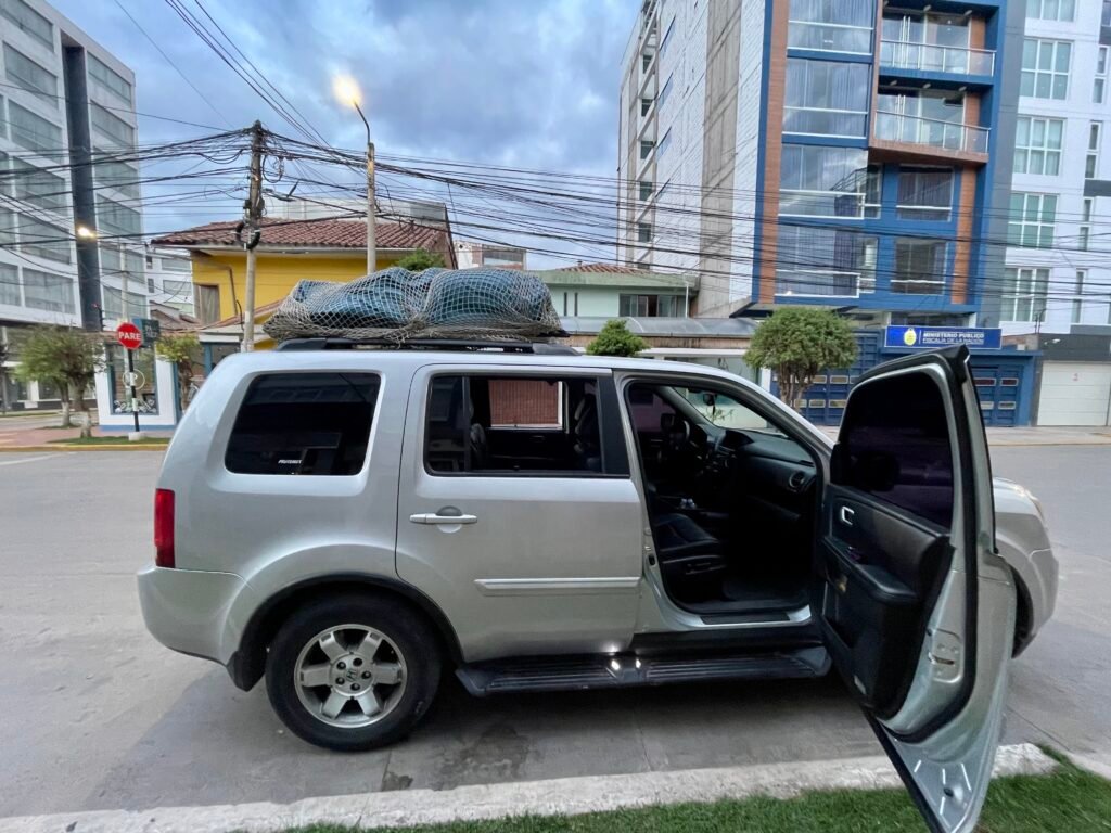 A silver Honda CR-V 4x4 parked on a narrow street in Cusco with the driver-side door open. The car is equipped for a long-distance road trip, illustrating the "boots on the ground" logistics of traversing the Andes.