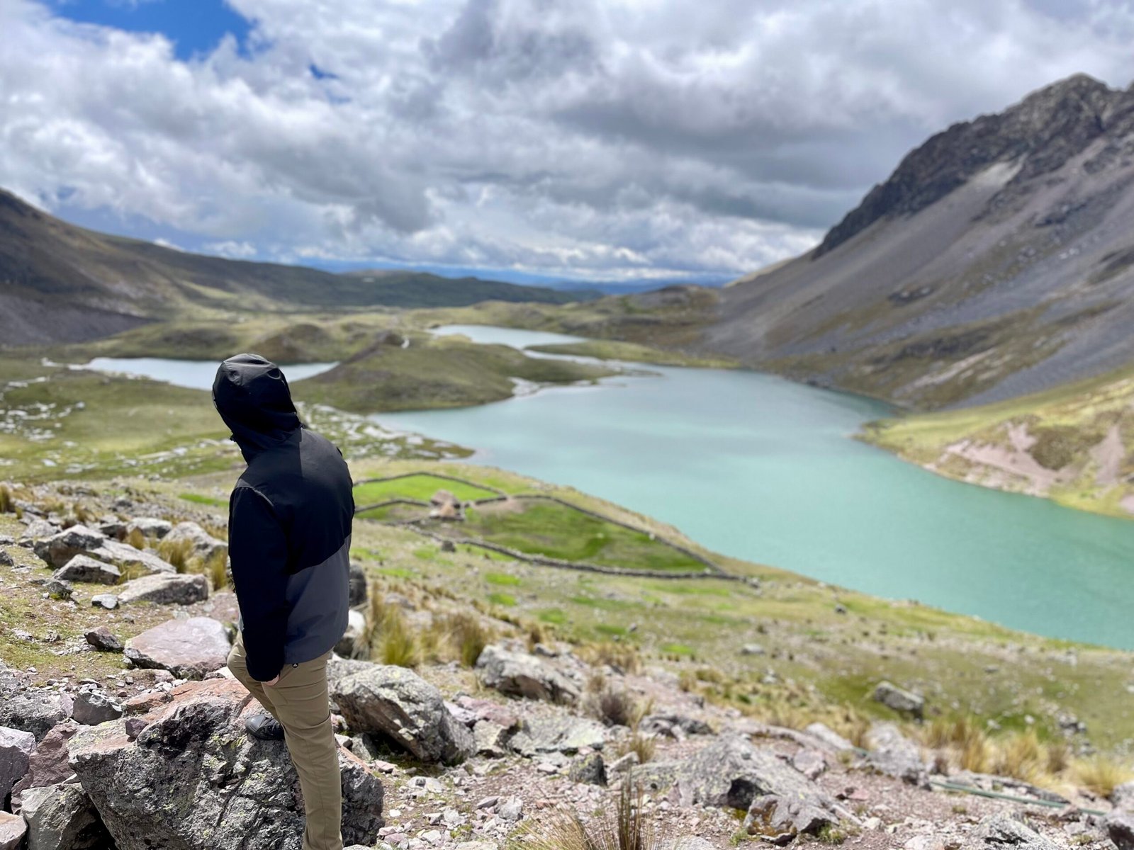 A high-angle view of a lone hiker overlooking the turquoise glacial lakes of Ausangate, representing the authentic and quiet experience of an overnight trekking expedition in Peru.