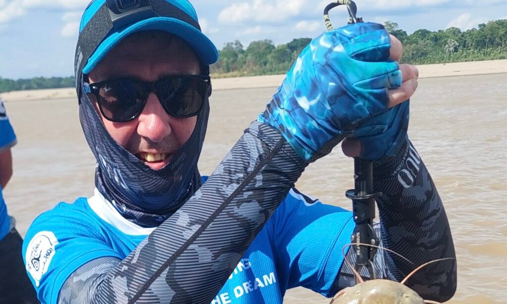 Traveler wearing protective moisture-wicking Lycra sleeves and face gear while fishing on a river boat in the Peruvian Amazon.