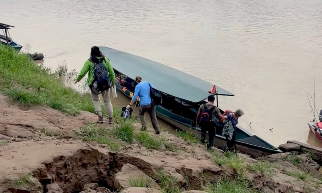 Travelers carefully navigating a steep, slick clay riverbank while boarding a motorized boat in the Peruvian Amazon.