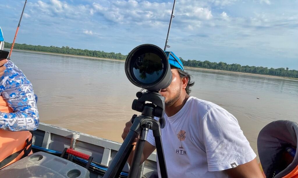 Marco, a local guide, using a spotting scope from a boat on a river in the Peruvian Amazon rainforest.