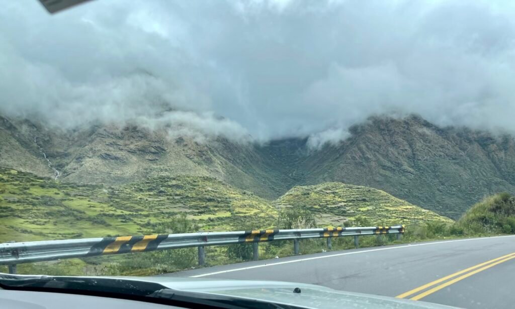 A view from the Interoceanic Highway in Peru showing a lush green mountain valley under a thick, flat, grey cloud ceiling during the 4,000-meter descent to the Amazon.