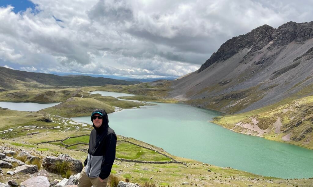 A traveler standing at a vantage point overlooking the turquoise 7 Lakes of Ausangate with glacier peaks in the background.