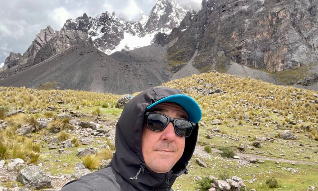 A traveler at a high-altitude shelter (5,000m) looking back toward the jagged ice walls of Ausangate, appearing physically exhausted.