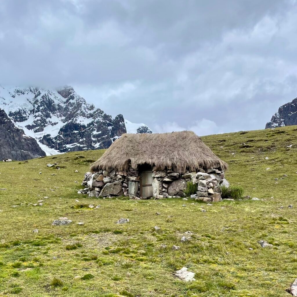 A traditional thatched-roof stone hut and horses used by local herders in the high-altitude landscape near the 7 lakes of Ausangate.