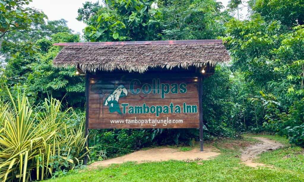 A wooden sign for Collpas Tambopata Inn located in the dense Peruvian rainforest.