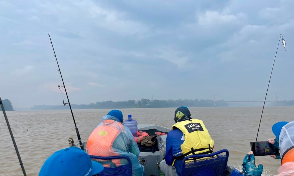 Travelers on a boat at the confluence of the Tambopata and Madre de Dios rivers in Puerto Maldonado during a rainstorm, with the Continental Bridge visible in the distance.