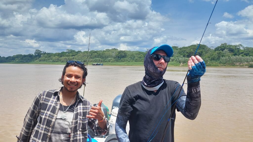A travel planner threading a fishing rod on the river alongside a local guide giving a thumbs up.