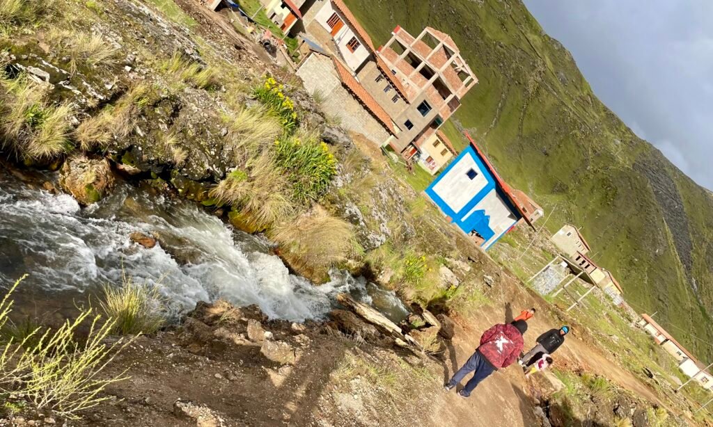A disorienting, tilted perspective of the high-altitude village of Pacchanta in Peru, showing raw stone paths and rushing water.