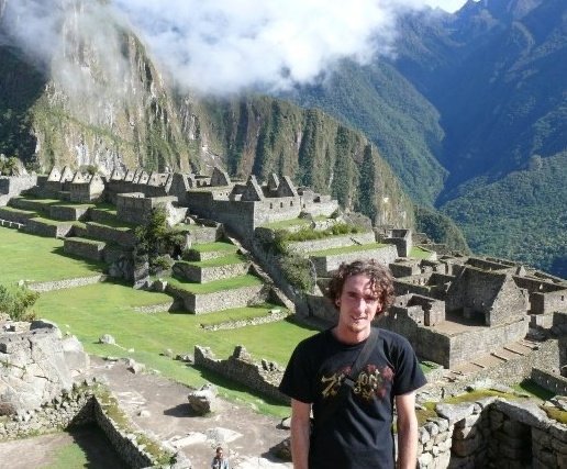 Kieran Proctor at Machu Picchu in 2007, standing in front of the empty stone ruins and agricultural terraces with no other tourists in sight under a cloudy Andean sky.