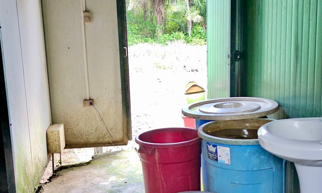 Logistics of jungle infrastructure, showing a rustic wash area and utility barrels in a Peruvian Amazon lodge.