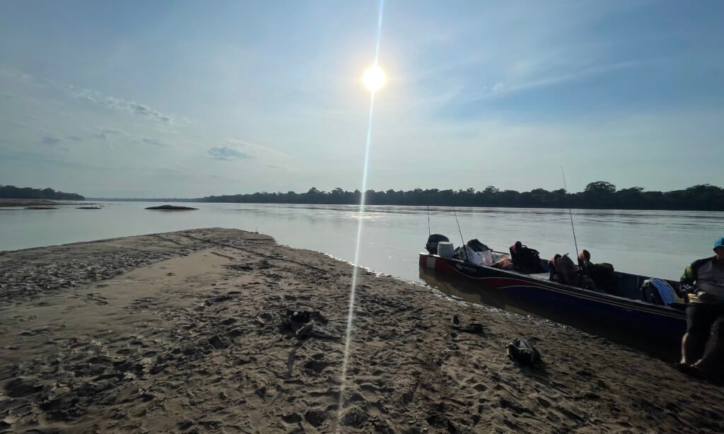 Logistics boat on a Madre de Dios river sandbar in Peru during the dry season, showing gear for remote jungle transit.