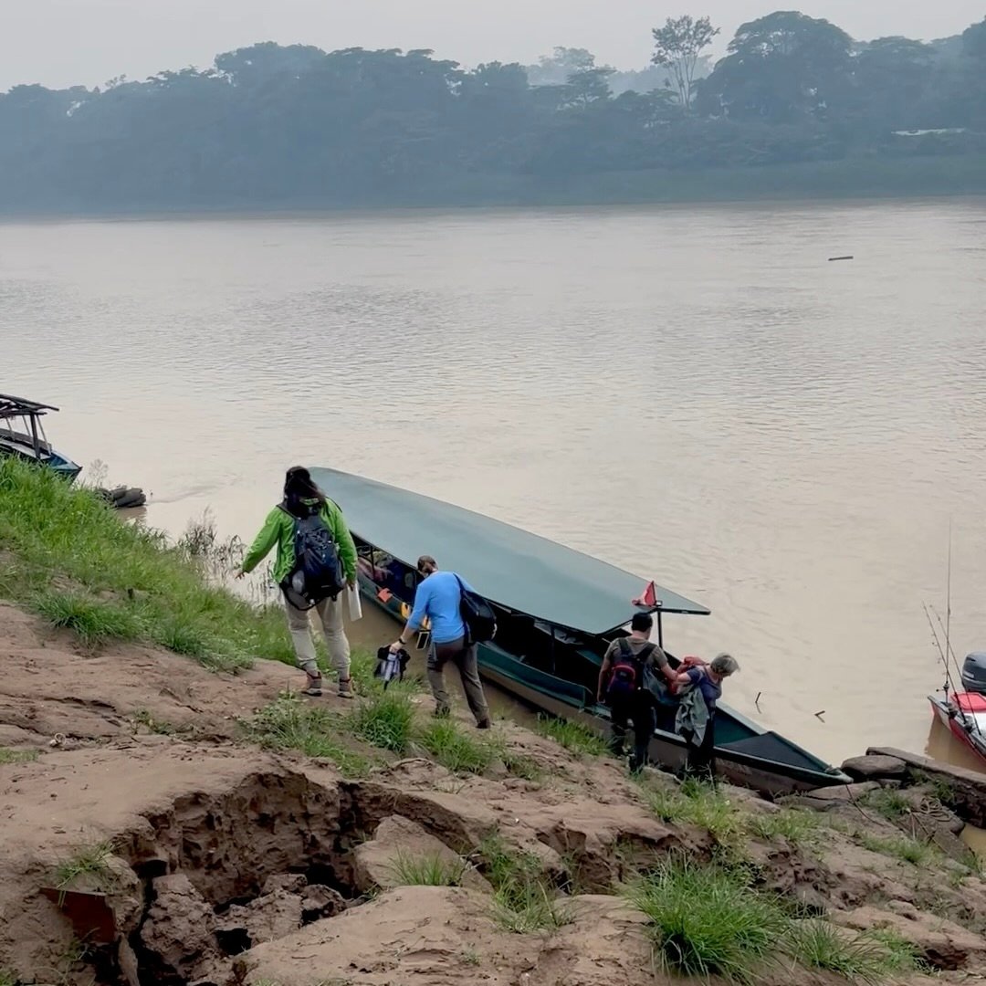 Travelers navigating a steep, muddy riverbank to board a motorized canoe in the Peruvian Amazon.
