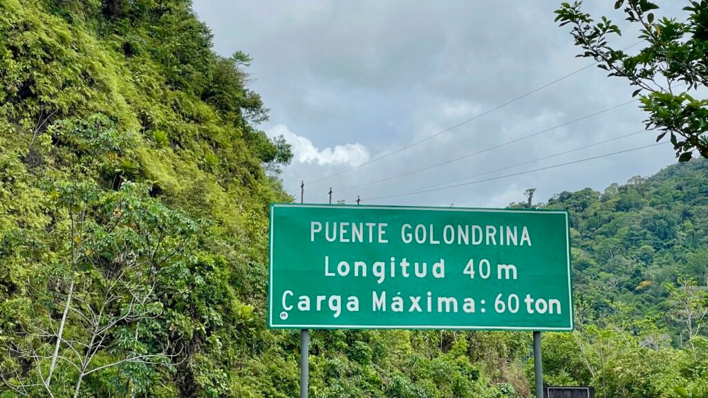 A green road sign for Puente Golondrina marking a 40-meter bridge in the Camanti district of Peru.