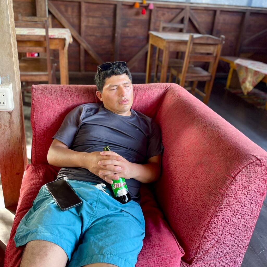 My friend Americo resting in a red armchair with a bottle of Pilsen beer during our night out in Puerto Maldonado.