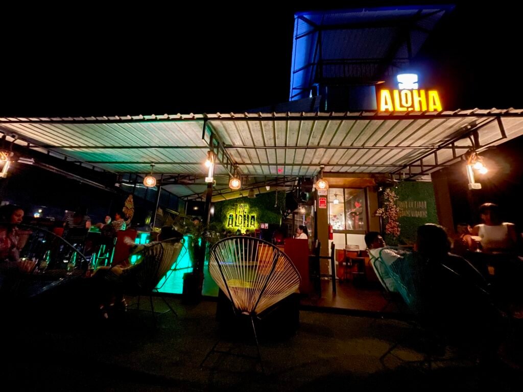 The rooftop Aloha bar in Puerto Maldonado at night with colorful lighting and outdoor seating.