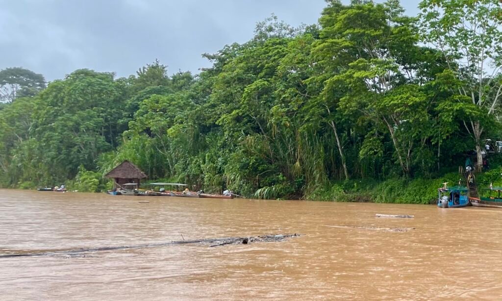 Rain-soaked river port of Filadelfia in Tambopata with wooden peque-peque boats used for lodge transfers.