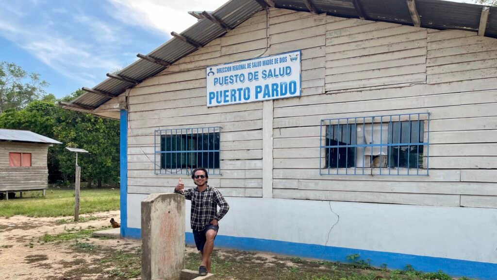 A traveler standing in front of the remote Puerto Pardo health post (Puesto de Salud) in the Madre de Dios region of the Peruvian Amazon.