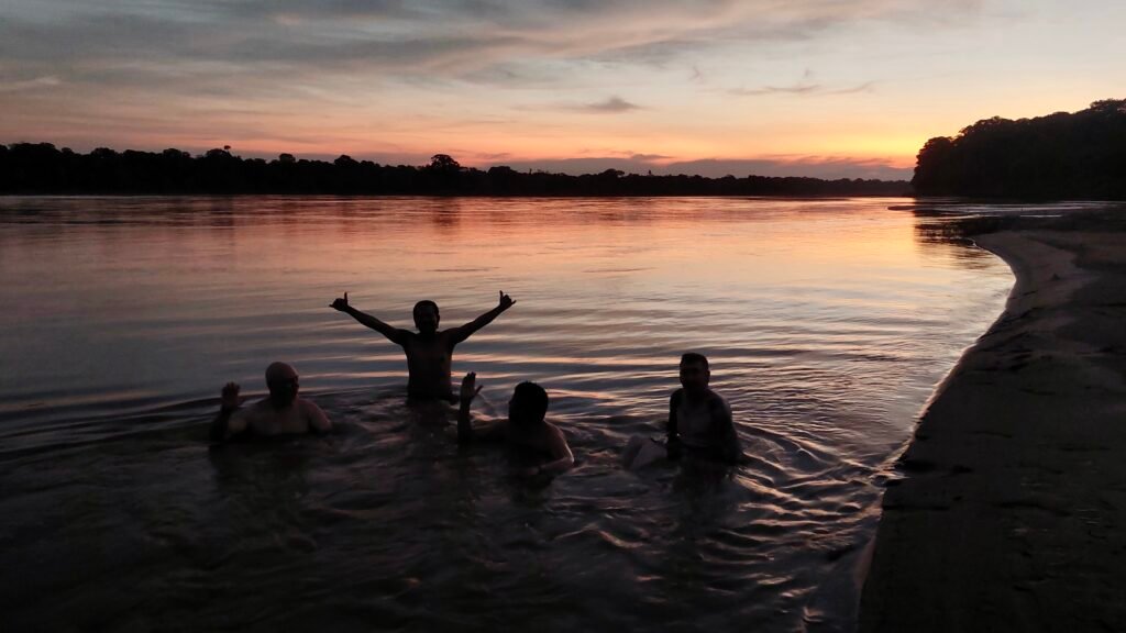 Travelers swimming in the Tambopata River during sunset in the Peruvian Amazon.