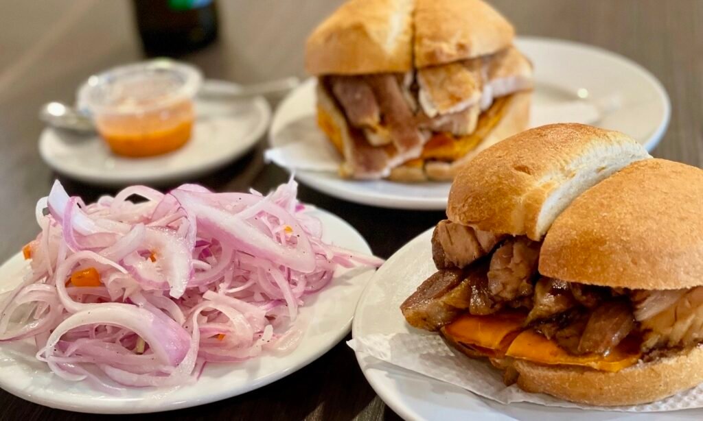 Close up of a traditional Peruvian pork sandwich with sliced red onions and salsa criolla.