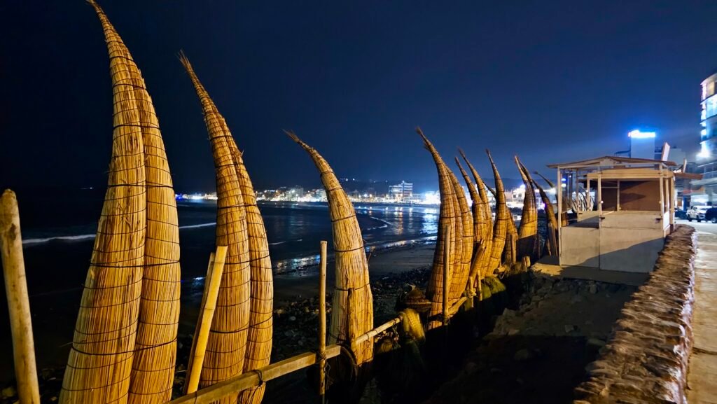 Traditional reed boats, or caballitos de totora, lined up on the Huanchaco beach at night with the town lights in the background.