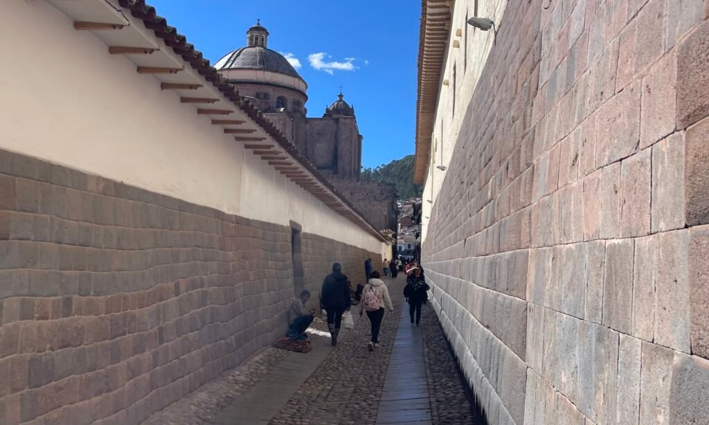 Close-up of historic Incan stone masonry foundations supporting colonial-era white-plastered buildings on a Cusco street.