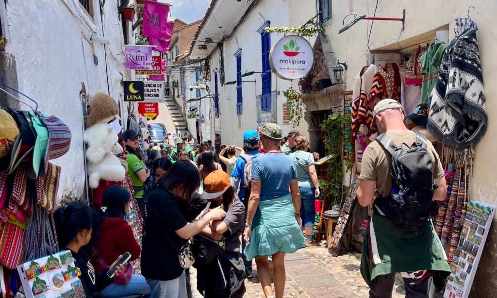 A busy, narrow street in Cusco lined with souvenir shops, tour touts, and tourist-oriented businesses between the Plaza de Armas and San Blas.