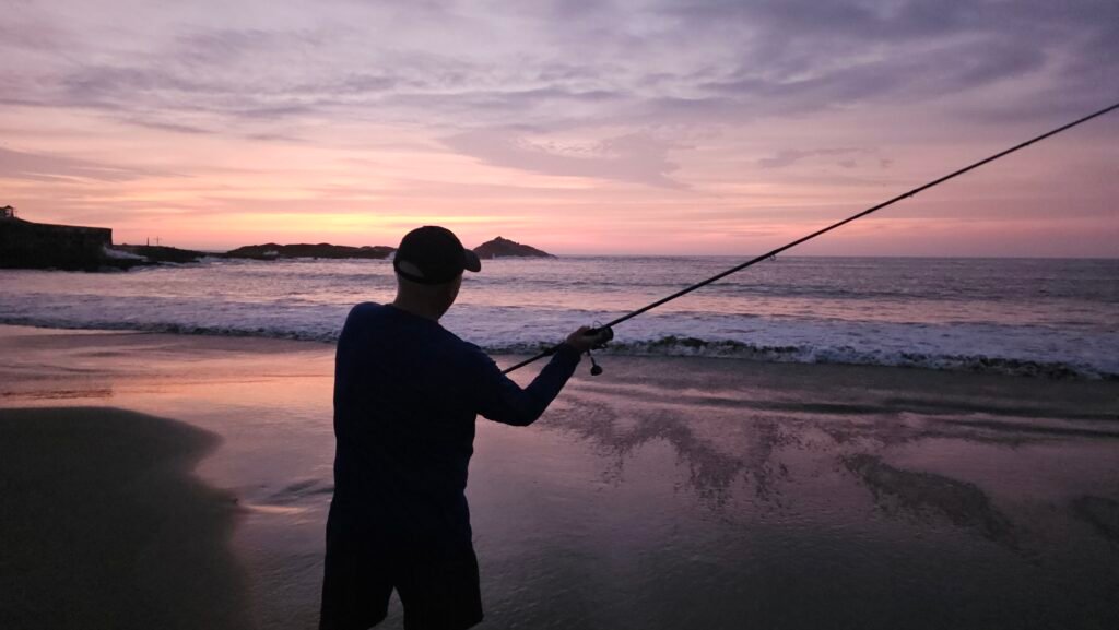 Dave from Canada fishing on the beach in Huarmey during a purple-hued sunset.