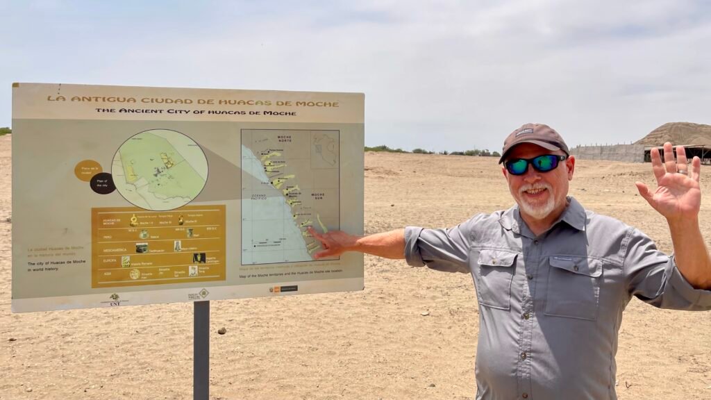 Dave pointing at an information sign explaining the locations of Moche archaeological sites along the Peruvian coast at the Huacas de Moche site near Trujillo.