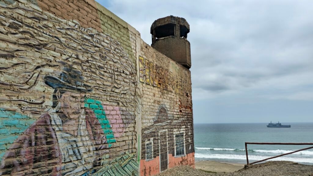 A weathered brick wall with local mural art overlooking the main beach and ocean in Huacho, Peru.