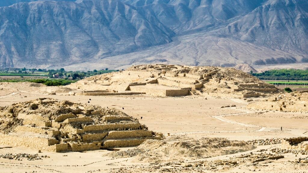 The ancient archaeological ruins of Caral, the oldest civilization in the Americas, set against a desert mountain landscape near Huacho, Peru.