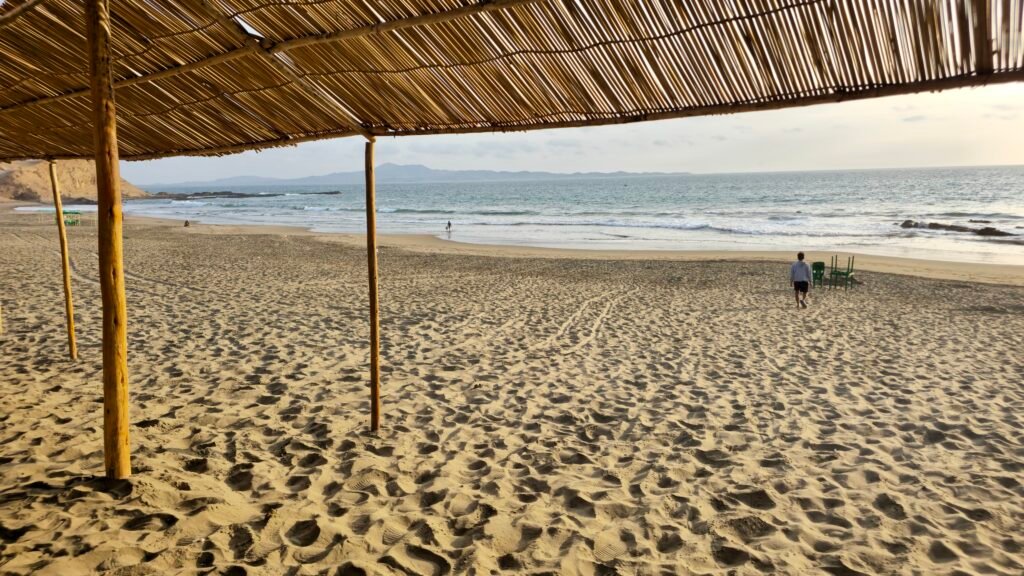 A beach waiter walking toward the water at Playa Colorado in Huacho, Peru, to set up a table and umbrella for a beachside meal.
