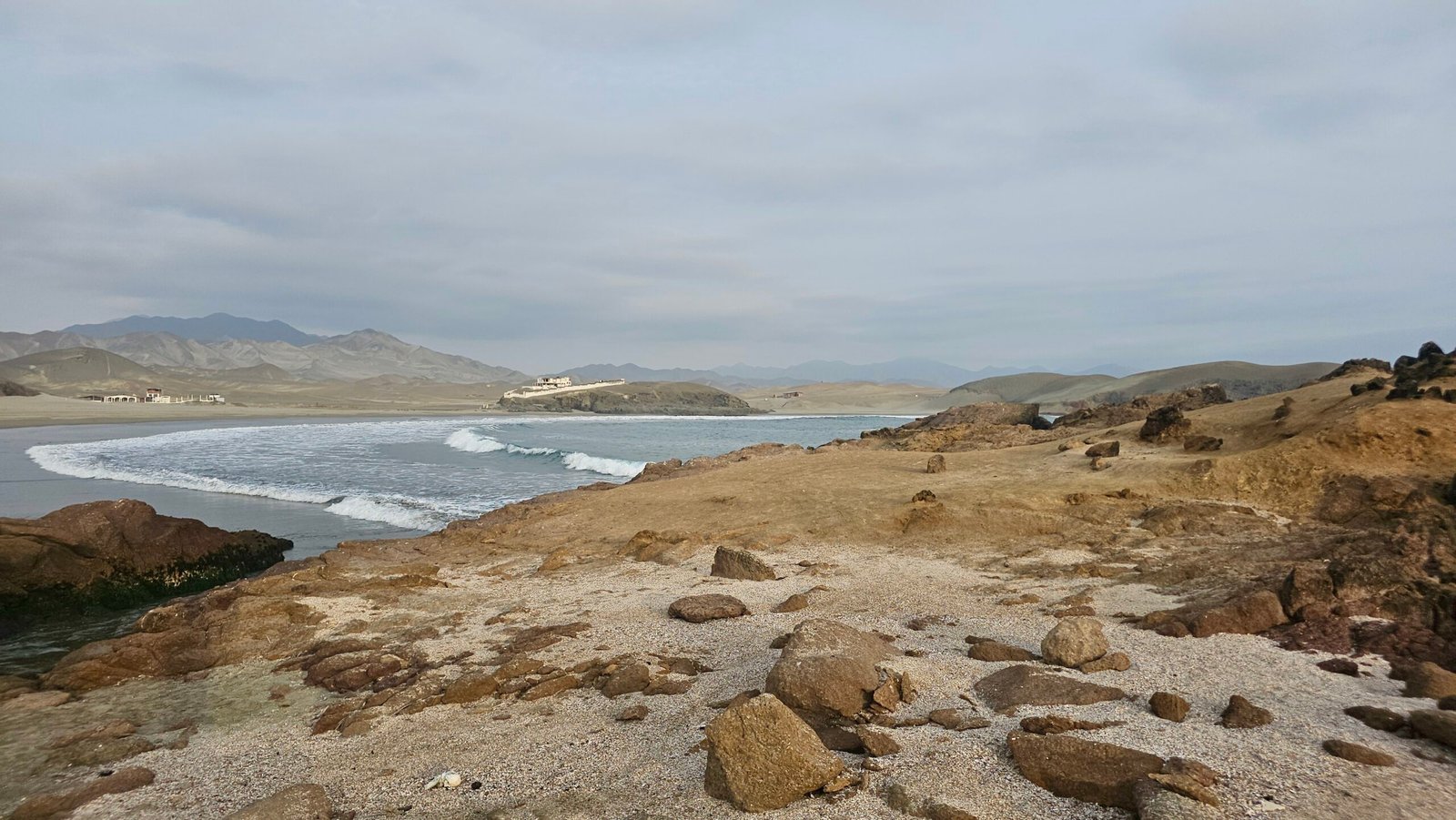 Rugged coastal landscape at Playa Tuquillo, showing the contrast between the sandy beach, arid hills, and the Pacific Ocean in Huarmey, Peru.
