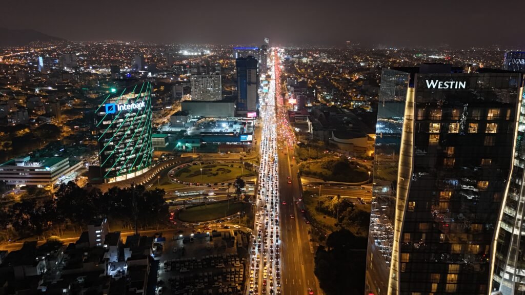 Aerial night view of heavy traffic on a major highway in Lima, Peru, featuring high-rise buildings and city lights.