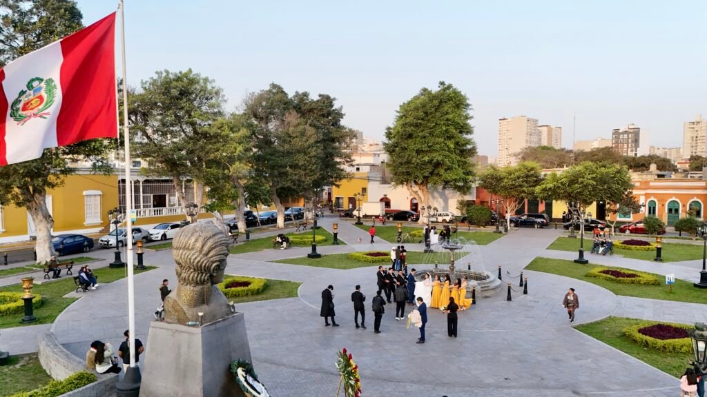 Aerial perspective of a public square in Lima with a bust in the foreground and the Peruvian flag.