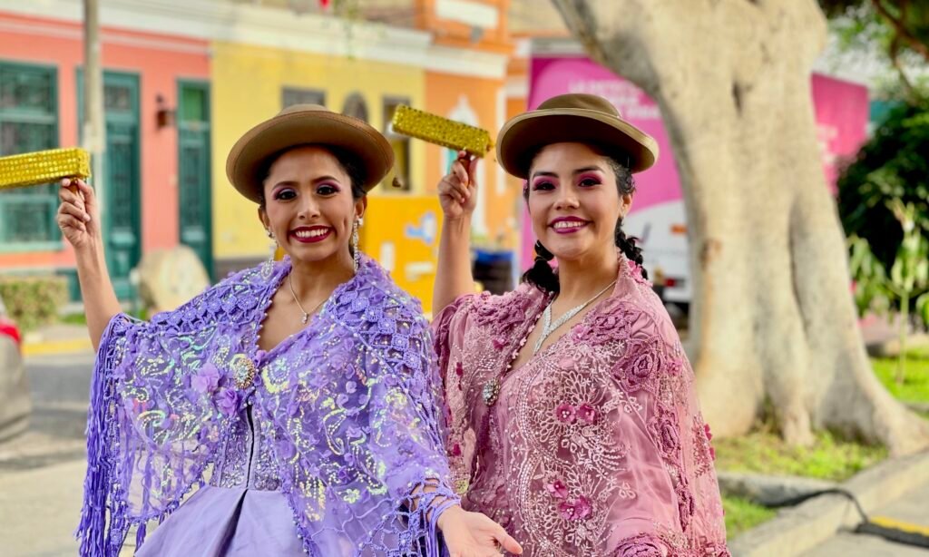 Two women in traditional Peruvian dance costumes holding gold rattles in Lima.