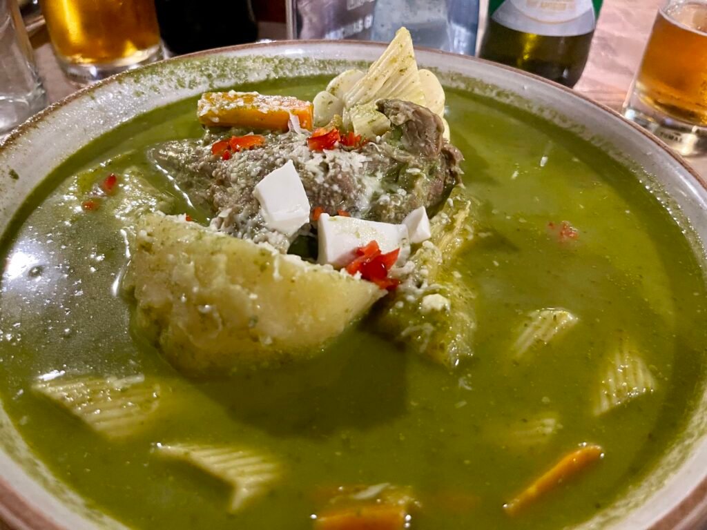 A vibrant green bowl of traditional Peruvian minestrone soup with vegetables and herbs.