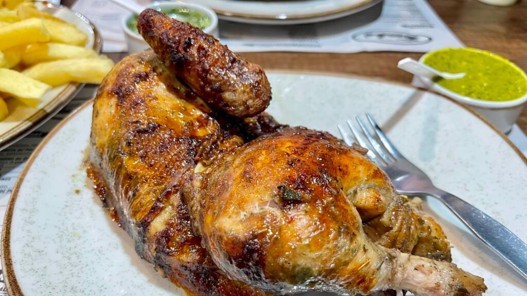 A golden-brown roasted Peruvian rotisserie chicken served with fries and green sauce.