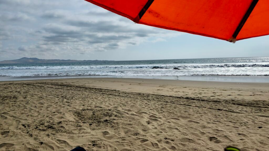 View from under a red beach umbrella looking out at the Pacific Ocean at Playa Colorado.