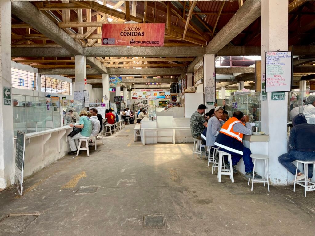 Local diners eating at a small, traditional food stall or huarique inside the San Blas Market in Cusco, Peru.